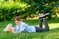 Very cute, young boy in round glasses and blue shirt reads book lying on the grass next to backpack and globe. Education Royalty Free Stock Photo