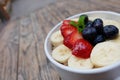 acai bowls with fresh fruit strawberry, blueberry, banana in white bowl on wooden table.