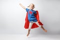 Very excited little girl dressed like superhero jumping alongside the white wall.