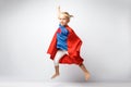 Very excited little girl dressed like superhero jumping alongside the white wall.