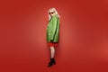 Very fashionable photo of a girl on a red background in flight. A blonde in a bright green raincoat, red glasses and a red dress