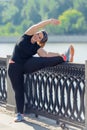 very flexible stout woman performs exercises on the embankment in the city park