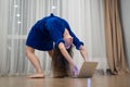 Very flexible woman exercising at home in front of her laptop, stretching her back. Concept of individuality, creativity