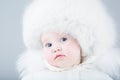 Very funny baby in a white snow suit and big fur hat Royalty Free Stock Photo