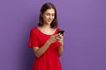 Very funny video. Cheerful young pretty brunette girl in red t-shirt sends text messages via mobile phone. Chatting with friend, Royalty Free Stock Photo