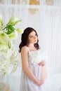 Very gentle pregnant girl in interior with flowers and tulle curtains