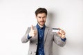 Very good bank. Businessman in suit show plastic credit card and thumb-up, recommending, standing on white background