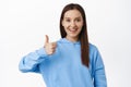 Very good. Image of young woman in hoodie showing thumb up in approval, like and agree, praise good work, satisfied with