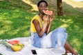 Very happy smiling black African woman sitting in an outdoor park while eating a watermelon and more fruit. Royalty Free Stock Photo