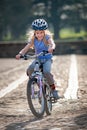 A very happy young blonde girl rides a bike along a cobbled path