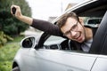 Very happy young man is peeking from the car window while looking at the camera. He is holding the keys at his right hand. Lottery