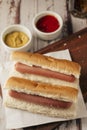 Very high view of a pair of hotdogs without garnishes with pots of mustard and ketchup on a rustic wooden tray. Vertical view