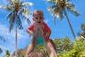 Very impressed baby little child raised high in arms against the sky and tropical palm trees. Infant Dressed in a coral and white