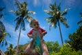 Very impressed baby little child raised high in arms against the sky and tropical palm trees. Infant Dressed in a coral and white