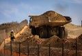 A very large haul dump truck at a construction site with a worker nearby