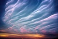 a very long cloud formation over a field at sunset or dawn with a windmill in the foreground and a blue sky with white clouds Royalty Free Stock Photo