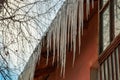 Very long icicles hanging from the slate roof above the window against a background of white clouds