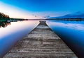 Very very long wooden bridge, almost to horizon, on the calm lake, summer sunset - blue rose skies reflected in still water. Royalty Free Stock Photo