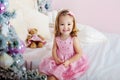 Very nice charming little girl blonde in pink dress sitting on a child`s bed and laughs loudly the background of Royalty Free Stock Photo