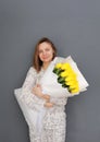 Very nice young woman holding big and beautiful blossoming bouquet of fresh yellow tulips flowers on the grey wall background. Royalty Free Stock Photo