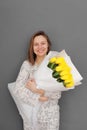 Very nice young woman holding big and beautiful blossoming bouquet of fresh yellow tulips flowers on the grey wall background. Royalty Free Stock Photo