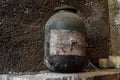 Very old and aged black jar covered with dust and spider web standing in front of the concrete wall at basement