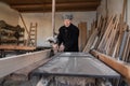 Very old man carpenter cutting wooden plank with circular saw in his workshop Royalty Free Stock Photo