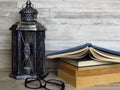 A very old silver lantern, a pile of old books, a pair of glasses on bleached oak background.