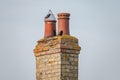 Very old twin chimney and pots seen atop a decaying and heavily weathered brick smokestack.