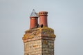 Very old twin chimney and pots seen atop a decaying and heavily weathered brick smokestack.