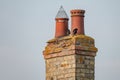 Very old twin chimney and pots seen atop a decaying and heavily weathered brick smokestack.