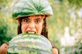 Very ridiculous girl writhes her face holding two halves of watermelon. Silly girl makes a funny face biting while