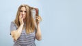 Very sad and upset young woman looking with shock at her damaged hair on blue background Royalty Free Stock Photo