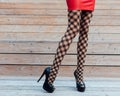 A very girl with long legs in fashionable, fishnet stockings, a short red leather skirt and black high-heeled shoes posing in Royalty Free Stock Photo