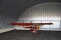 Very small single-place ultralight glider stands in the corner of a metal hangar