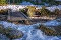 Very small wooden flat bridge over forest creek much water flowing under it. Melting snow in forest close to the running water Royalty Free Stock Photo