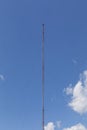 Very tall, thin radio station transmission antenna against a blue sky with clouds