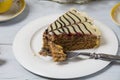 Very tasty piece of cake cut with a fork on a white plate and a cup of coffee in yellow on a light wooden table. The process of Royalty Free Stock Photo