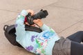 A very young female photographer lays on her back while using a large DSLR camera to get the perfect angle