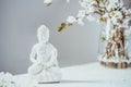 Decorative white Buddha statuette with blooing tree branches in the vase on the white background. Meditation and Royalty Free Stock Photo