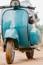 Vespa Scooter front close up view, parked in a muddy road in a rainy day. Sky blue vintage classic motor bike