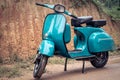 Vespa Scooter front view, parked in a muddy road in a rainy day. Sky blue vintage classic motor bike.Vespa Scooter front view,