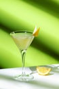 Vesper cocktail drink with dry gin, vodka, aperitif, lemon zest and ice in martini glass. Light green background, hard light, Royalty Free Stock Photo