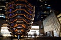 Vessel TKA, a spiral endless staircase with the Shed near it, skyscrappers behind. Night view with bright lights. Hudson Yards