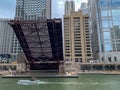 Vessels motors underneat a raised drawbridge as pedestrians watch on Chicago River