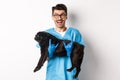 Vet clinic concept. Happy male doctor veterinarian holding cute black pug dog, smiling at camera, showing rock-n-roll Royalty Free Stock Photo