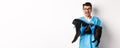 Vet clinic concept. Happy male doctor veterinarian holding cute black pug dog, smiling at camera, showing rock-n-roll Royalty Free Stock Photo