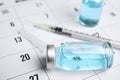 Vial and syringe on calendar, closeup. Vaccination and immunization