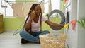 Vibrant african american woman passionately engaged in conversation on smartphone while washing clothes in busy home laundry room