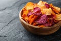 A vibrant assortment of baked vegetable chips served in a rustic wooden bowl on a dark slate background Royalty Free Stock Photo